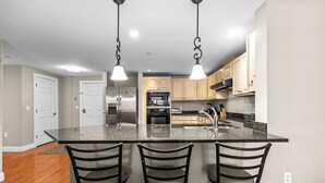 A kitchen with a central island, bar stools, stainless steel appliances, and light-colored cabinets. - Grand Victorian unit 309, 3 bedrooms (Old Orchard Beach)
