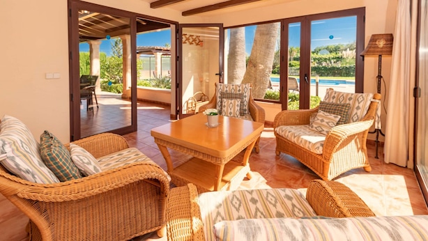 A spacious living area with wicker furniture, a wooden coffee table, and large windows offering a view of the outdoors. - 3 bedroom villa, with private pool and BBQ, Pollensa (Pollensa)