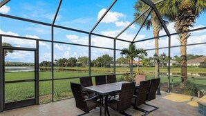 Een overdekt terras met een tafel en stoelen, grote glasramen en uitzicht op een groen landschap.