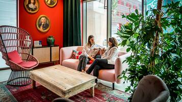 Un intérieur moderne avec un mur d’accent rouge, un fauteuil en osier, une table basse en bois et une grande fenêtre donnant sur les bâtiments environnants.