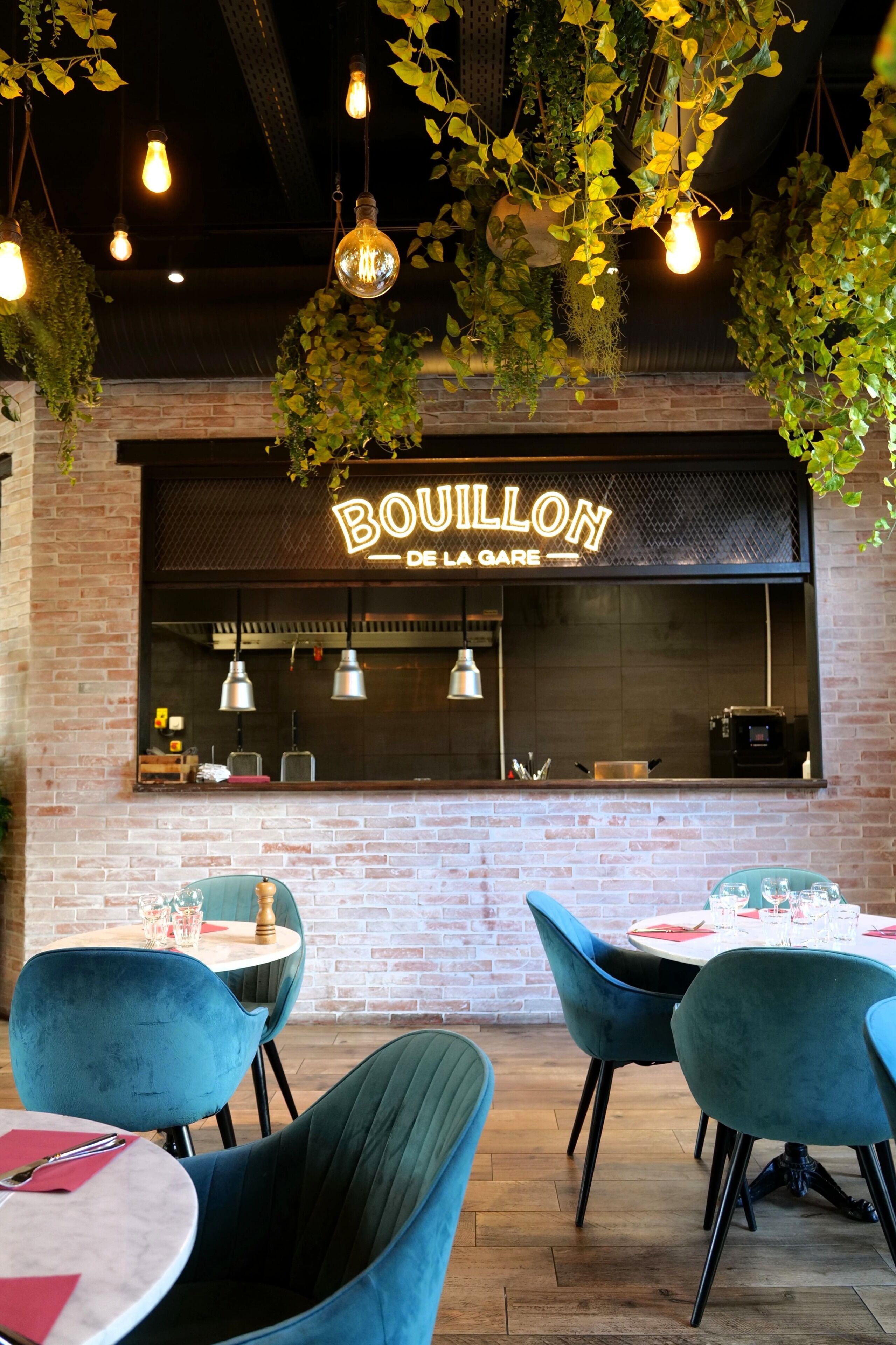 A restaurant interior with hanging plants, exposed brick walls, and blue chairs.