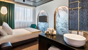 Una habitación de hotel moderna con cama, tocador con un espejo grande y ventana con cortinas.