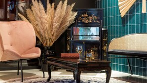 Una habitación con una silla rosa, una mesa negra con un libro y un vaso, y una estantería con objetos decorativos.