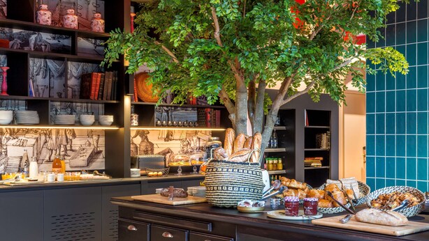 Un área de bufé con diversos alimentos, un árbol decorativo y una estantería con libros y adornos.