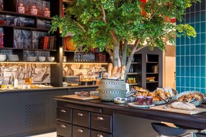 A buffet area with a variety of food items, a decorative tree, and a bookshelf with books and decorative items. - Aiden by Best Western Lorient Centre (Lorient)