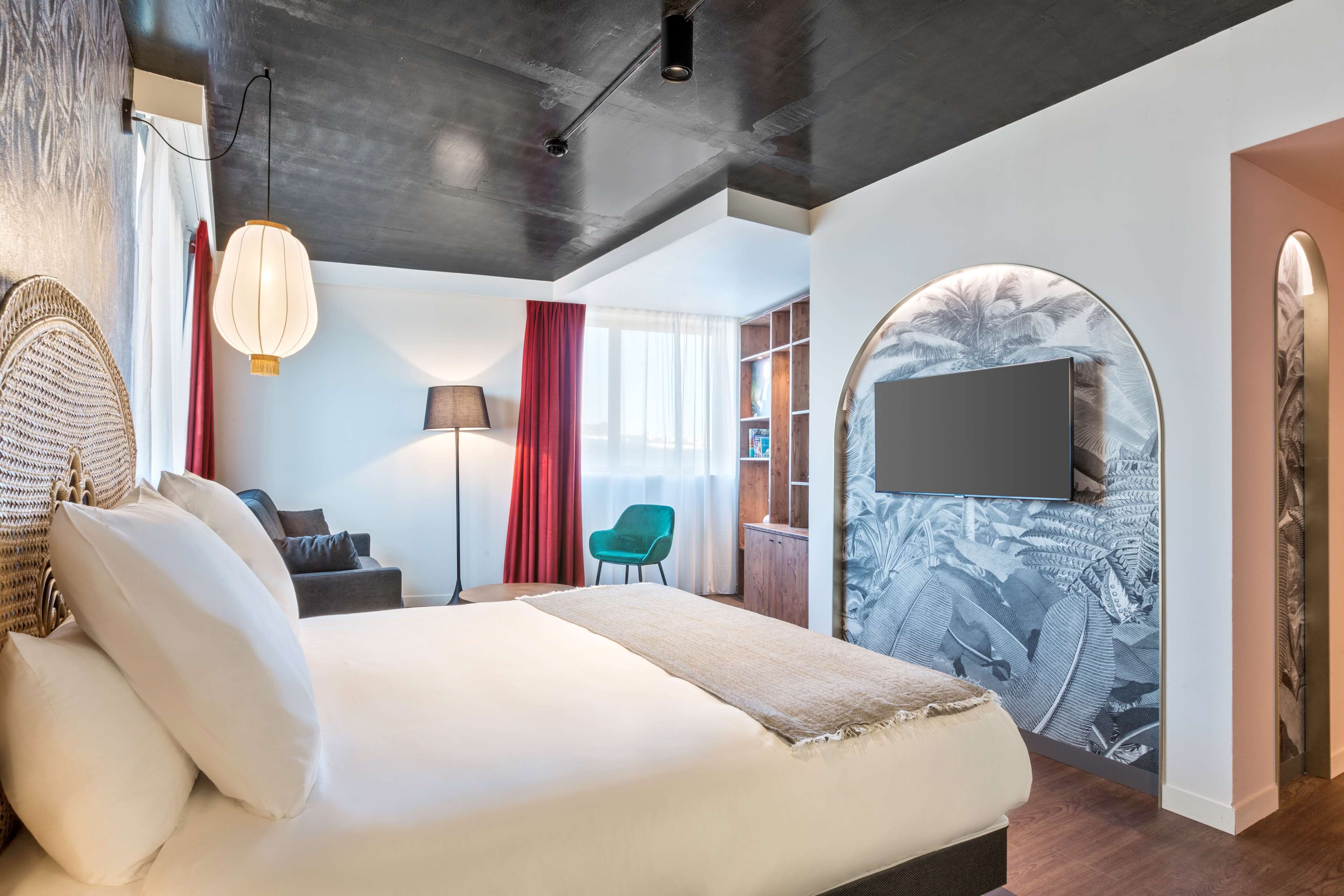 Una habitación de hotel moderna con una cama grande, un televisor de pantalla plana en la pared, un escritorio con una silla y una estantería.