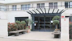 Un bâtiment moderne doté d’une entrée en verre, d’un espace d’attente abrité et de plantes en pot.