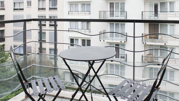 Un balcon avec une table et des chaises, donnant sur une rangée d’immeubles d ’habitation blancs.