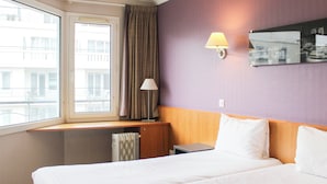 Une chambre d’hôtel avec un grand lit, un bureau, une lampe et une fenêtre avec des rideaux.