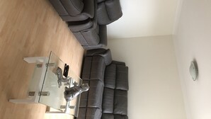 Uma sala de estar moderna com um sofá seccional cinza escuro, uma mesa de centro de vidro com pequenas figuras de animais decorativas, e um design minimalista.