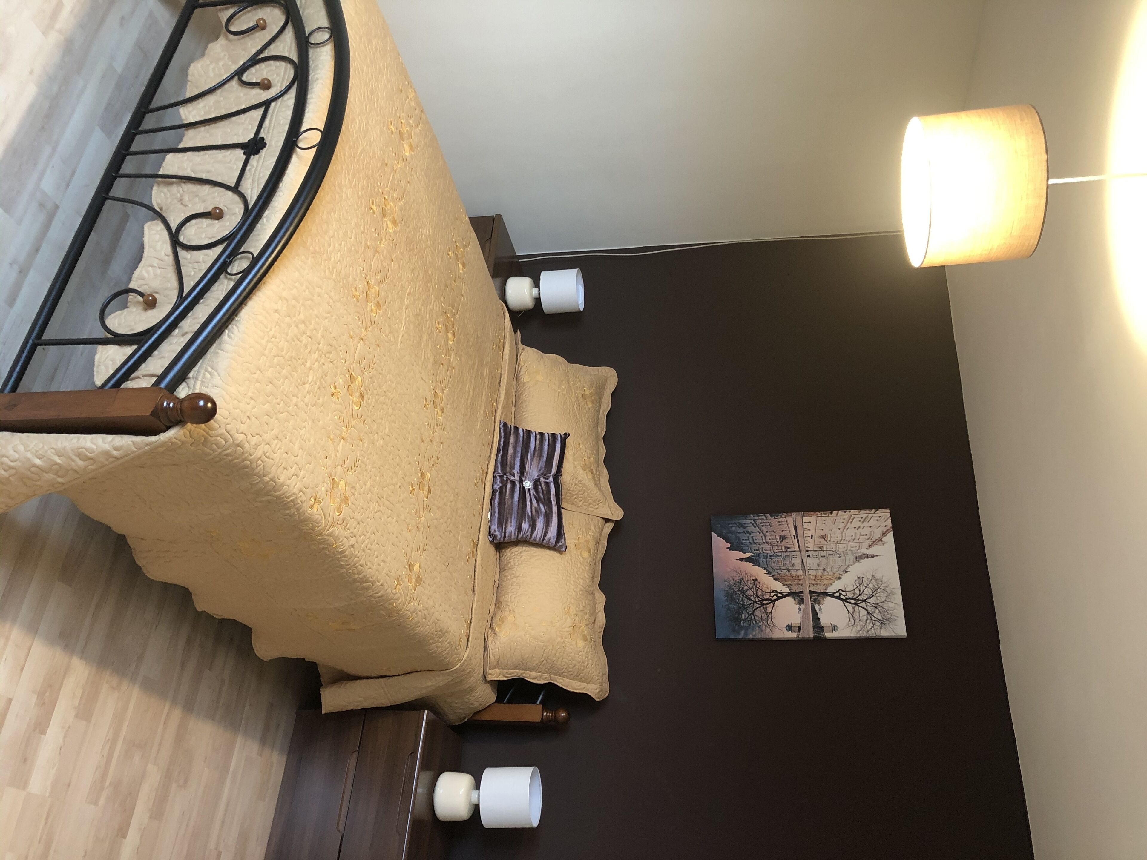 Ein Zimmer mit einem Bett, einem Wandbild und einer Stehlampe.