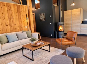 A modern living room with a sofa, coffee table, ottoman, and leather chair. A fireplace is visible in the background. - Modern Chalet With Garden Chamonix (Chamonix-Mont-Blanc)