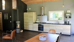 A modern kitchen with a central island, wooden cabinets, and a large window providing natural light. - Modern Chalet With Garden Chamonix (Chamonix-Mont-Blanc)