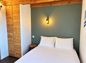 A bedroom with a bed, a nightstand, a wall-mounted light, and wooden paneling on the wall.