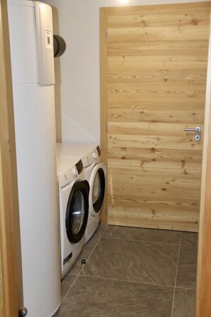 A compact laundry area with a washing machine and dryer, a wooden door, and tiled flooring.