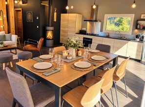 A modern kitchen with a wood stove, dining table set for six, and a view of the outdoors. - Modern Chalet With Garden Chamonix (Chamonix-Mont-Blanc)