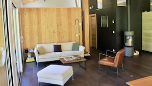 A modern living room with a wooden ceiling, a white sofa, a leather chair, and a fireplace. - Modern Chalet With Garden Chamonix (Chamonix-Mont-Blanc)