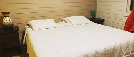 A bed with white bedding in a room with wooden walls and a small painting above it.