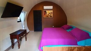Quarto com cama, escrivaninha, cadeira, televisão na parede e porta.