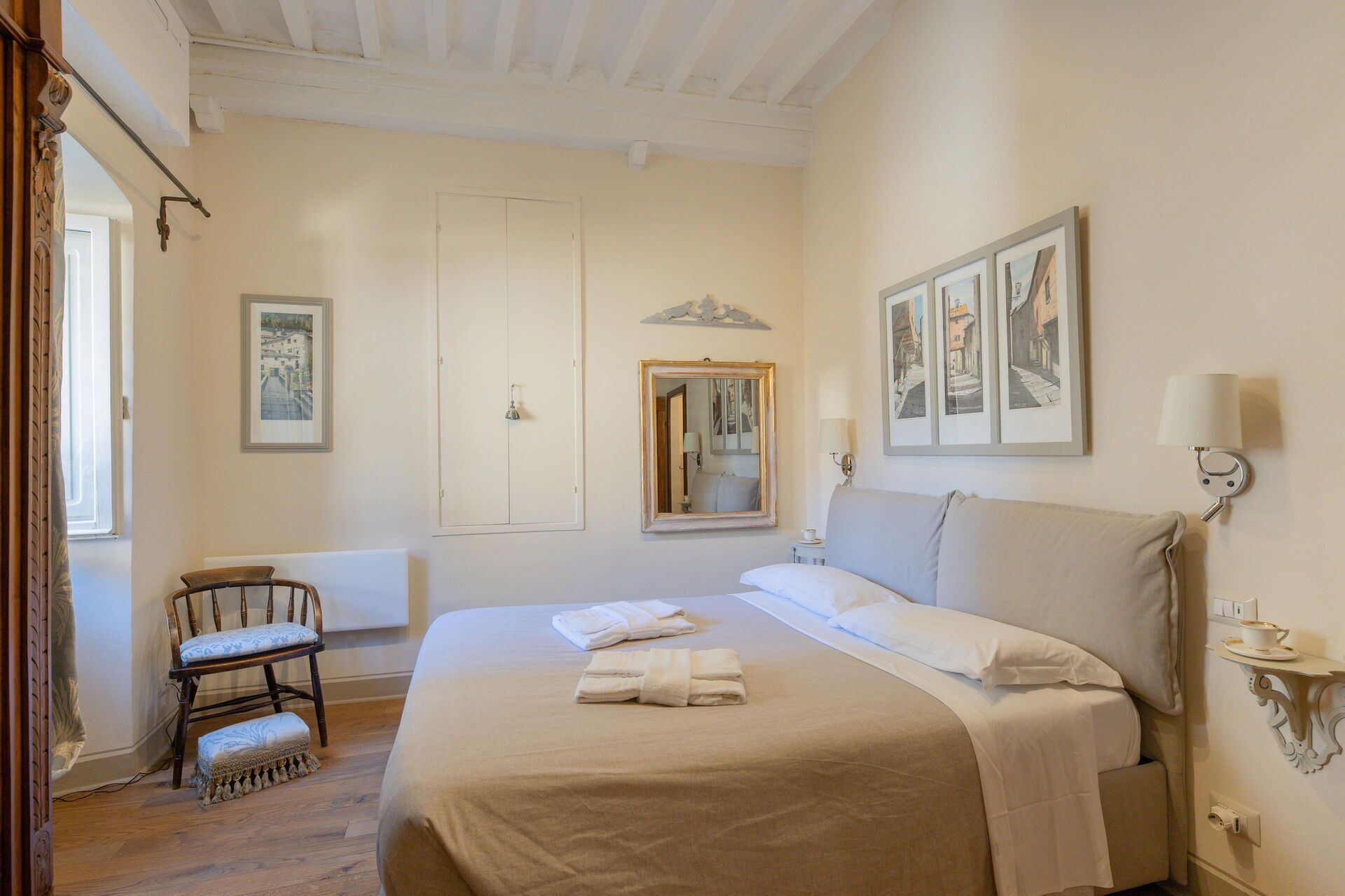 Une chambre d’hôtel avec un grand lit, une chaise, un miroir et des œuvres d’art accrochées aux murs.