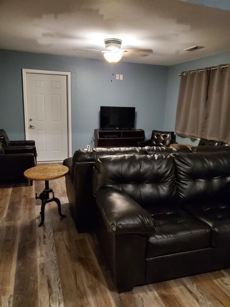 A living room with a black leather sofa, a small round table, a ceiling fan, and a television.