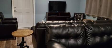 A living room with a black leather sofa, a small round table, a ceiling fan, and a television.