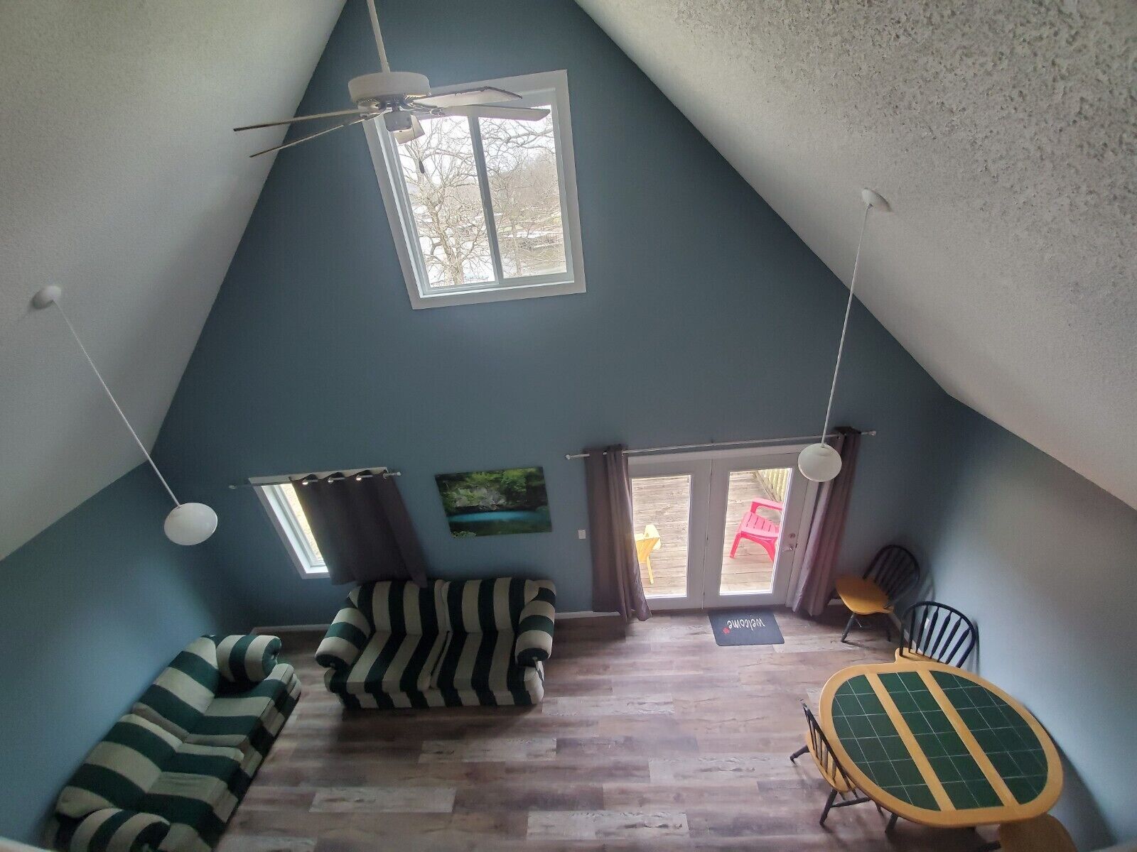 A cozy attic room with a sloped ceiling, a ceiling fan, a window, a sofa, a chair, and a small table.
