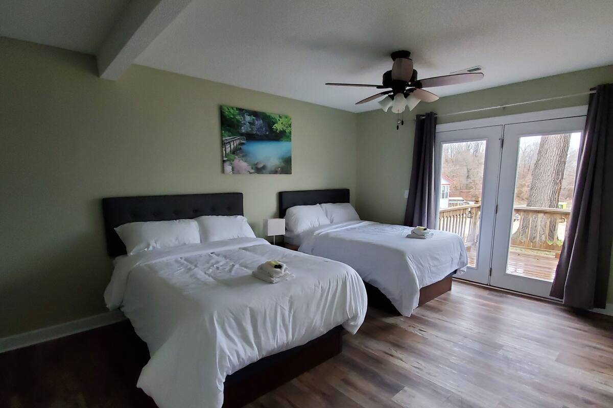 Habitación de hotel con dos camas, un ventilador de techo y un ventanal con vistas al exterior.