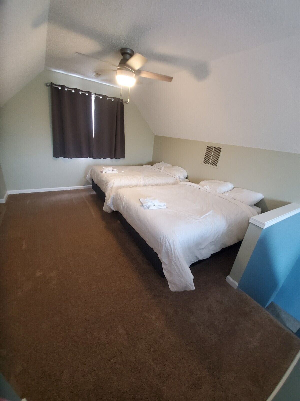 A room with two beds, a ceiling fan, a window with curtains, and a carpeted floor.