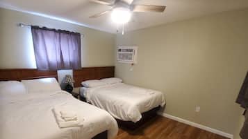 A hotel room with two beds, a ceiling fan, an air conditioning unit, and wooden flooring.