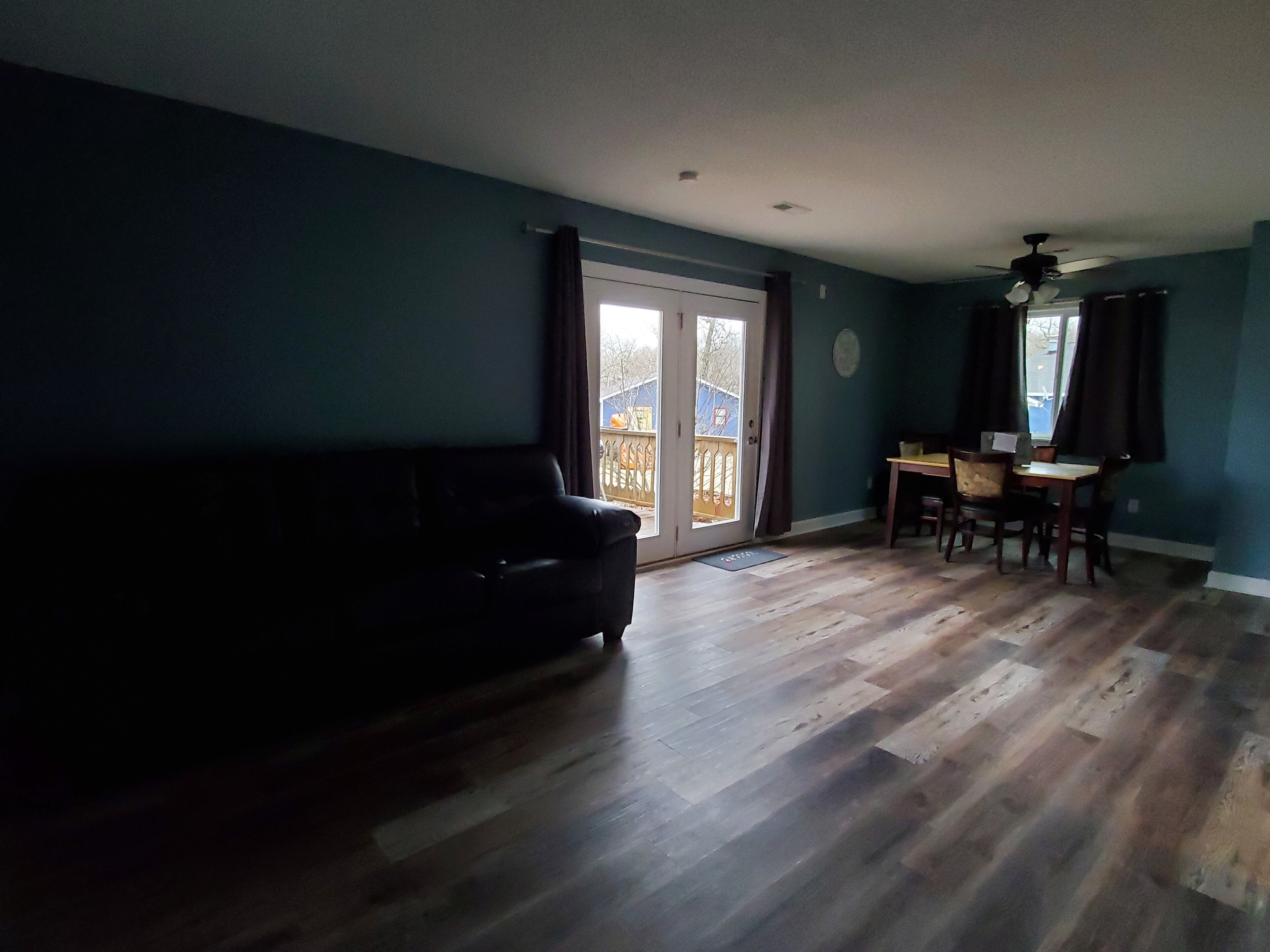 Un salon avec un canapé aux couleurs sombres, une table à manger avec des chaises et une porte-fenêtre coulissante donnant sur un espace extérieur.