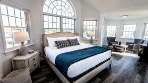 Un dormitorio amplio con una cama grande, varias ventanas, un rincón de descanso y vistas al exterior.