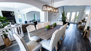 Un comedor amplio con una gran mesa de madera rodeada de sillas tapizadas, un candelabro y plantas en macetas.
