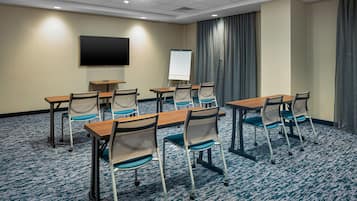 A conference room with a large table, chairs, a whiteboard, and a TV on the wall.