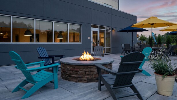 An outdoor seating area with Adirondack chairs, a stone fire pit, and yellow umbrellas. - Fairfield Inn & Suites by Marriott Somerset (Somerset)