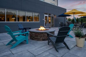 An outdoor seating area with Adirondack chairs, a stone fire pit, and yellow umbrellas.