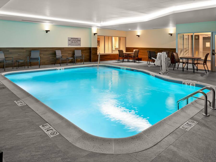 An indoor swimming pool with a tiled floor, lounge chairs, and a table with chairs.