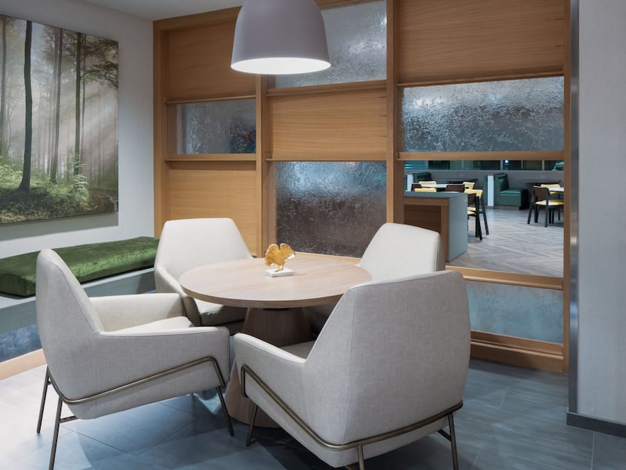 Una sala de reuniones moderna con una mesa redonda, cuatro sillas, un banco verde y un ventanal con vista al comedor.