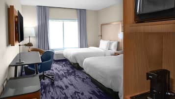 Habitación de hotel con dos camas, un escritorio, una silla, un televisor, una cafetera y una ventana con cortinas.