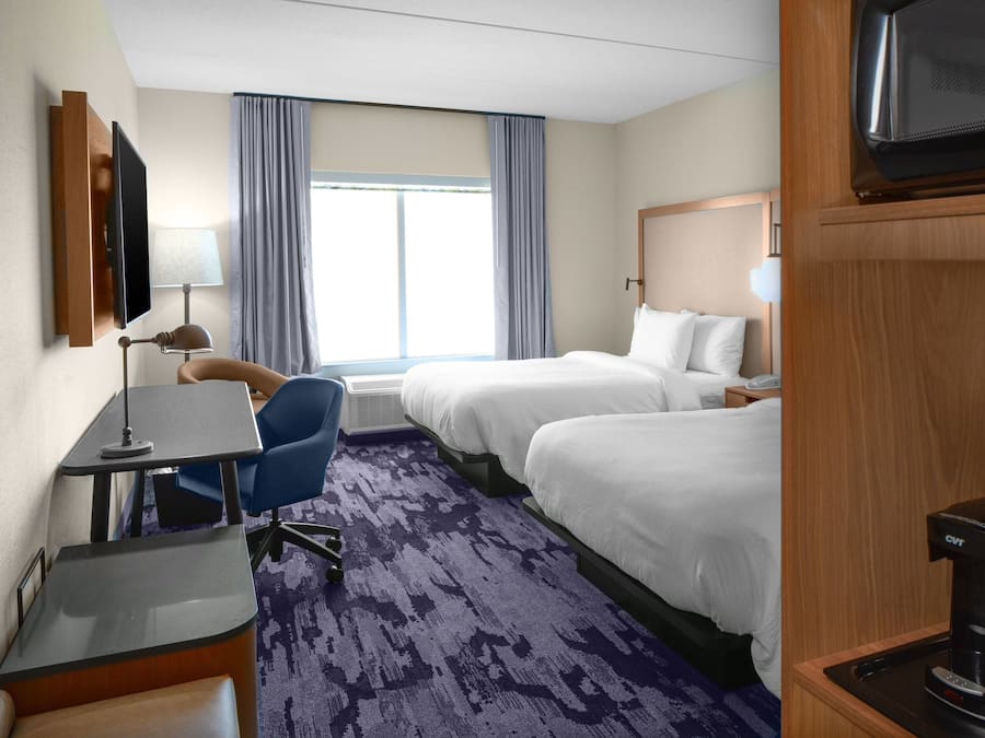 Habitación de hotel con dos camas, un escritorio, una silla, un televisor, una cafetera y una ventana con cortinas.