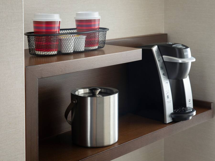 A kitchen counter with a coffee maker, a kettle, and a basket containing two striped cups.