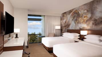 Une chambre d’hôtel avec deux lits, un bureau, une chaise, une télévision et une grande fenêtre donnant sur un beau paysage.