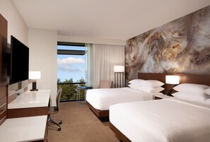 A hotel room with two beds, a desk, a chair, a TV, and a large window with a view.