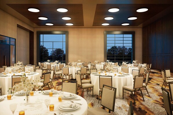 Un salón de banquetes con mesas redondas, sillas y centros de mesa florales.