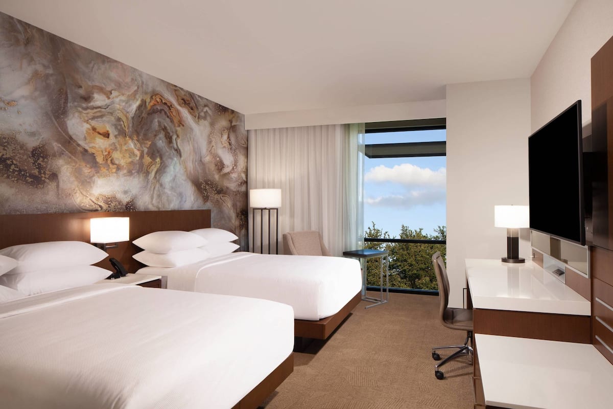 Une chambre d’hôtel avec deux lits, un bureau, une chaise, une télévision et une grande fenêtre donnant sur un beau paysage.