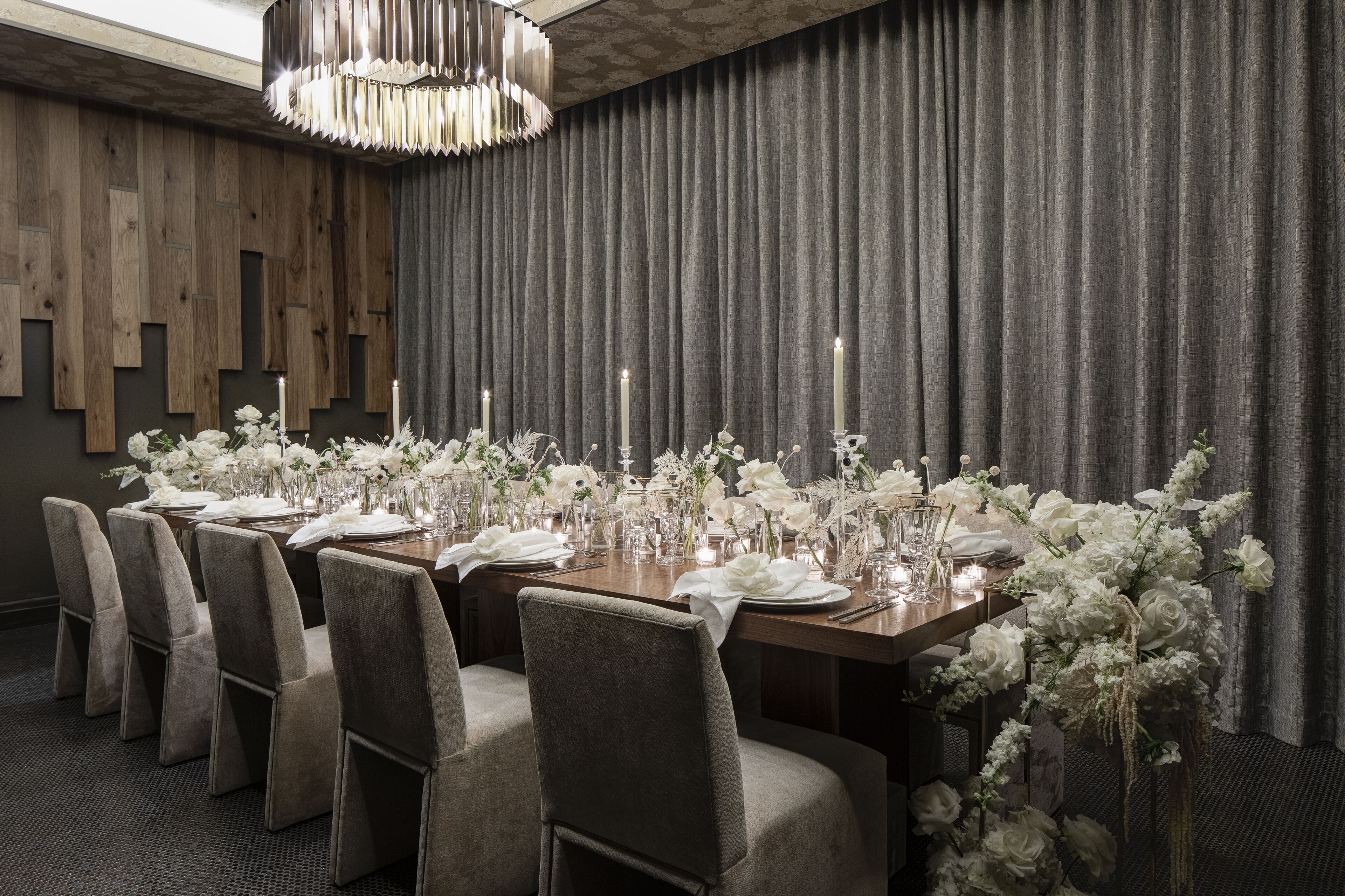 A dining area with a long table set for six, surrounded by grey upholstered chairs.