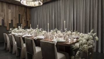 A dining area with a long table set for six, surrounded by grey upholstered chairs.