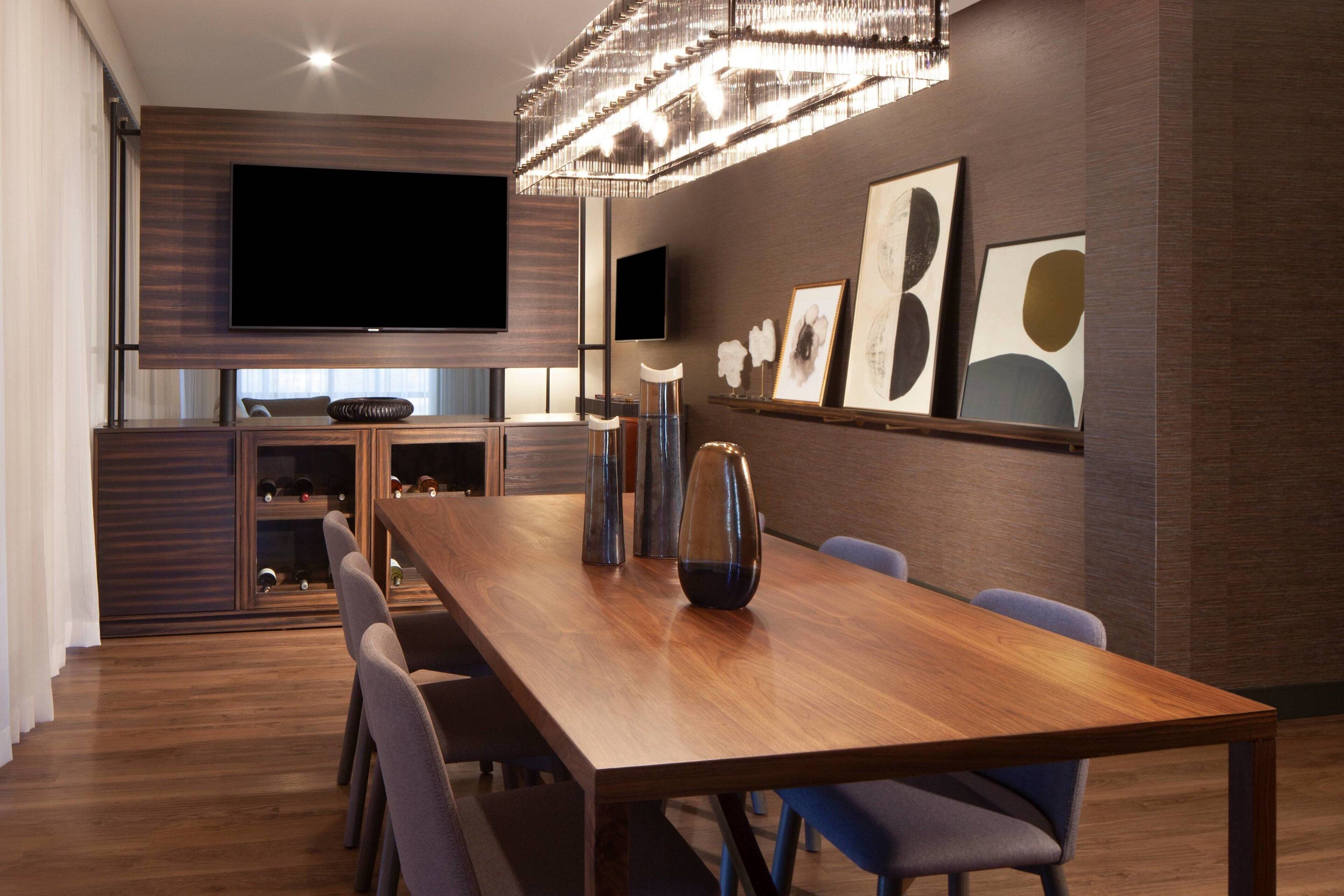 Zona pranzo moderna con tavolo in legno, sedie, un lampadario e opere d'arte alle pareti.
