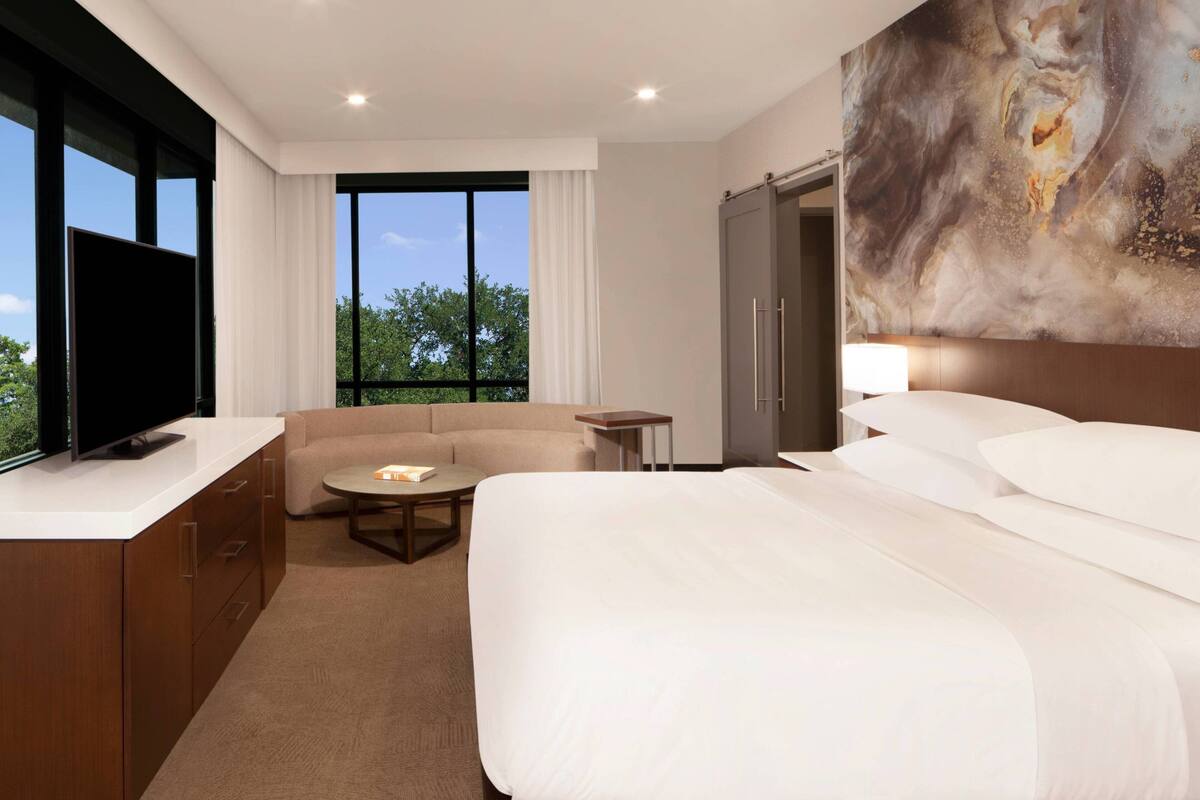 Une chambre d’hôtel avec un lit, une télévision, un canapé, une petite table et un tableau au mur.