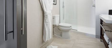 A modern bathroom with a toilet, shower, and a robe hanging on the wall.